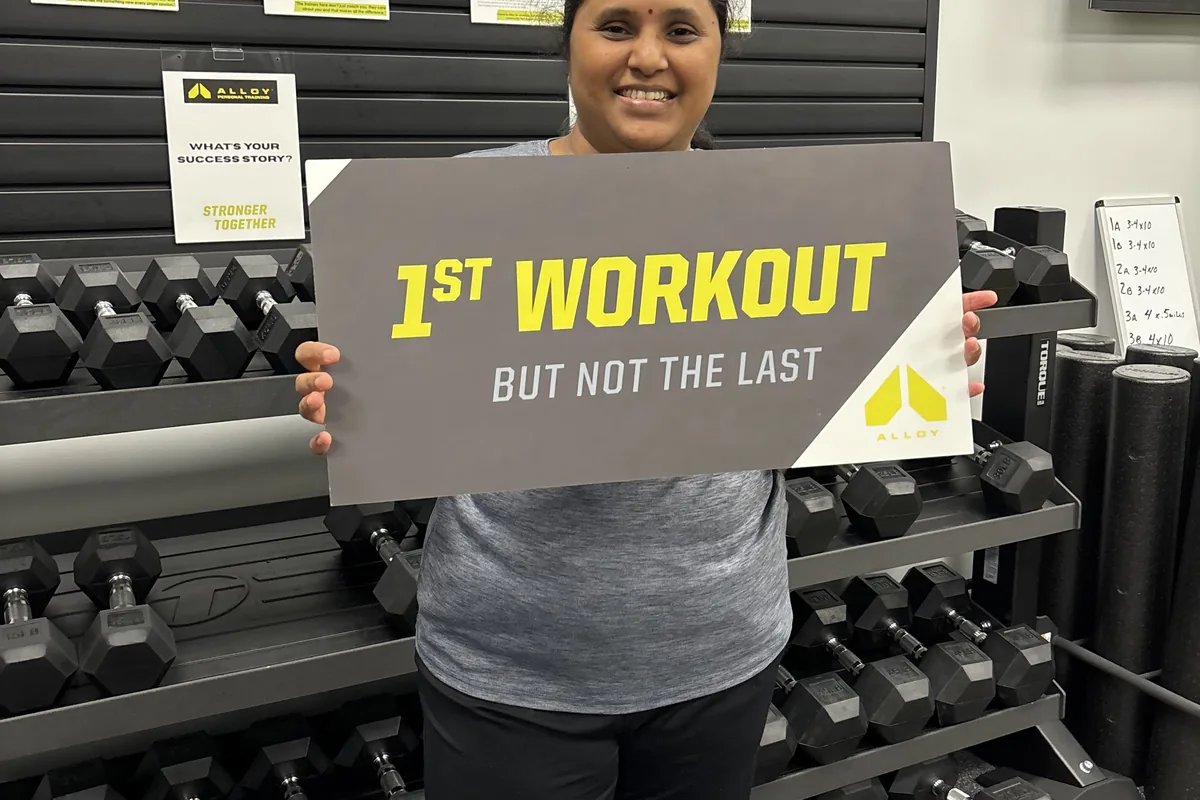 Alloy Cary member holding a first-workout milestone sign